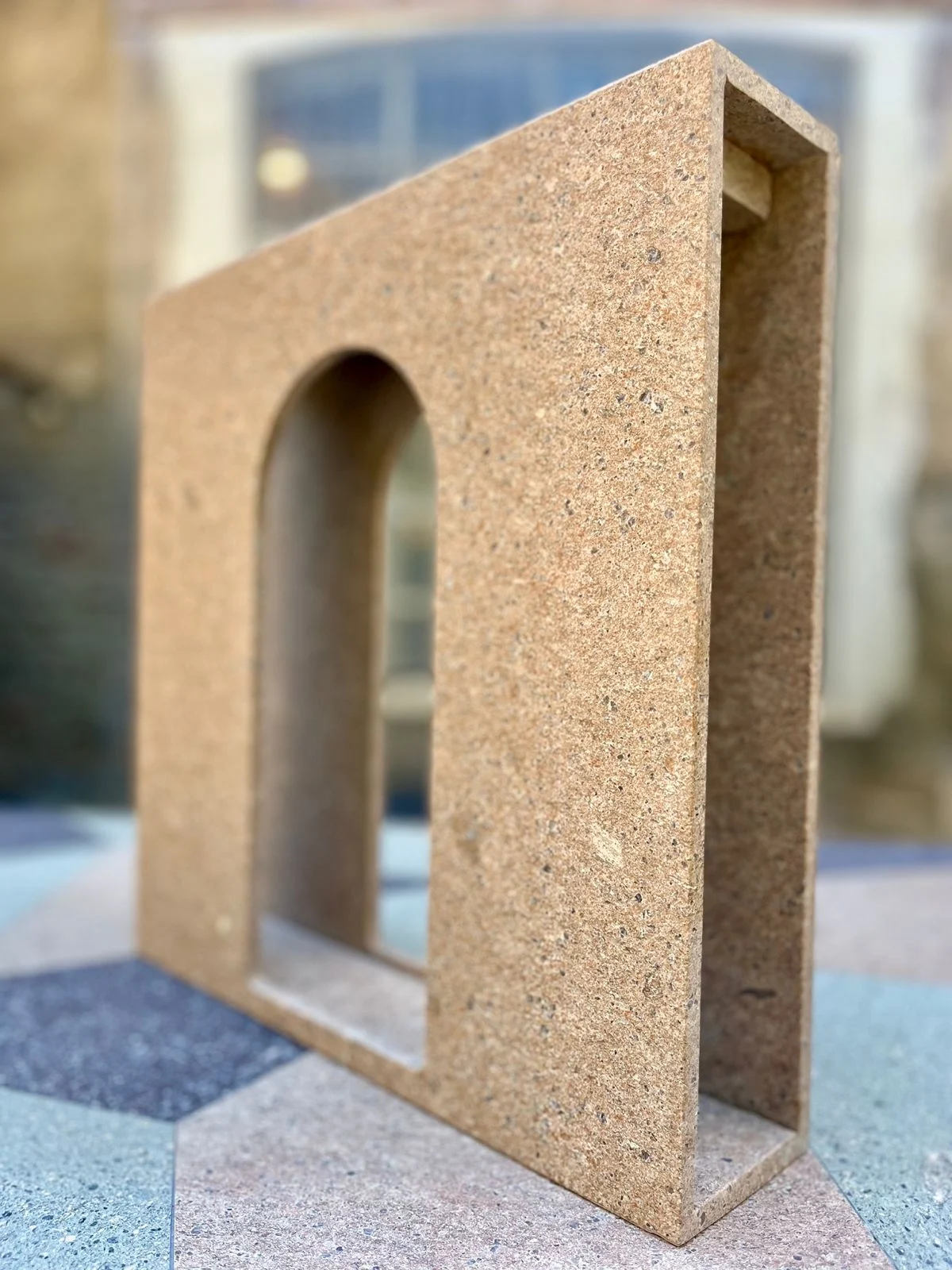 Elemento a mensola in porfido ocra con un'apertura ad arco, su un pavimento in pietra a motivi geometrici – Collezione Frammenti per Porfido Pedretti, Milano, Italia, 2025 – design di prodotto