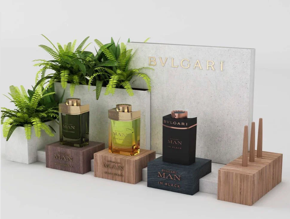 Render di un espositore da banco Bvlgari Man: tre flaconi su blocchi di legno davanti a un pannello in cemento e felci – Bvlgari Man Wood Neroli, 2019 – retail design