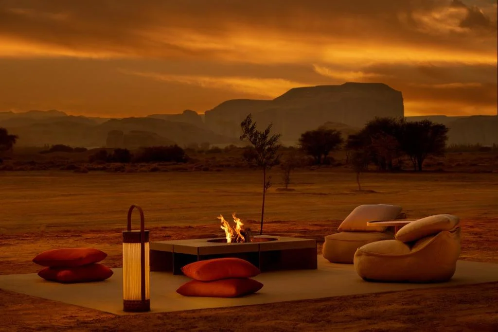 Lanterna accanto a un braciere e a sedute lounge nel deserto al tramonto, formazioni rocciose dietro – Lanterna AlUla per Artemide, Milano, Italia, 2025 – lighting design