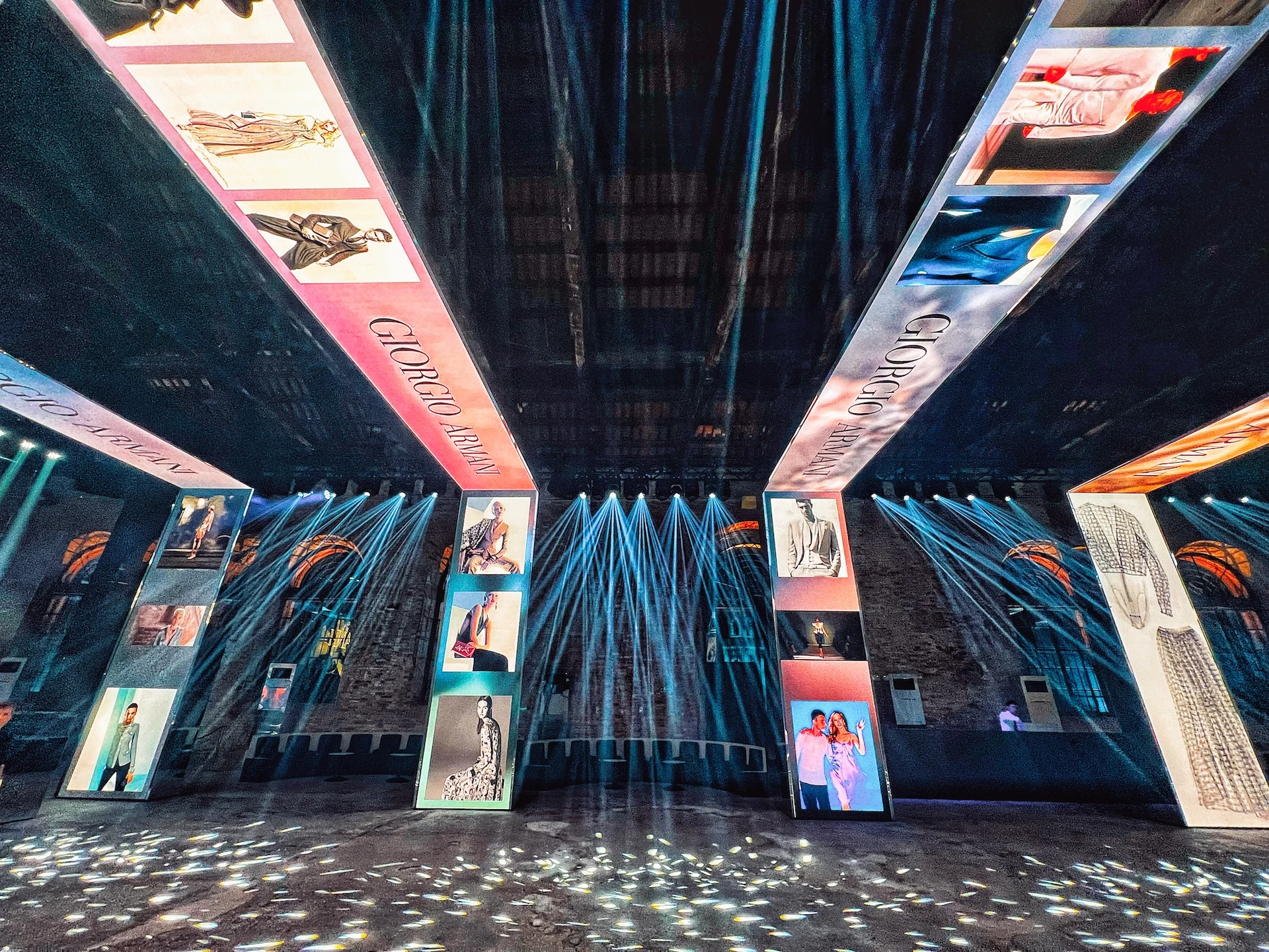 Vista dal basso dei portali LED con immagini di moda, fasci di luce blu a ventaglio nella sala in mattoni – Festa Armani/Archivio alla Mostra del Cinema di Venezia, Italia, 2025 – progettazione di eventi