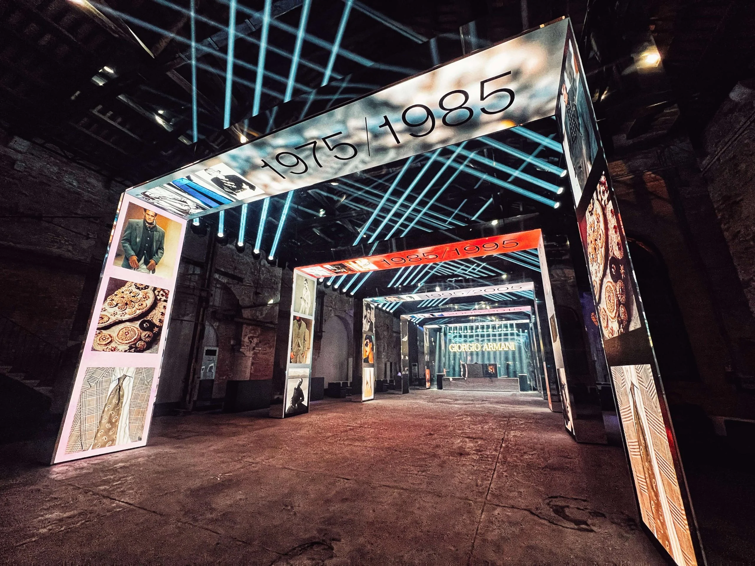 Portale LED con la scritta 1975/1985 che si apre su una sequenza di portali dei decenni, barre di luce blu in alto – Festa Armani/Archivio alla Mostra del Cinema di Venezia, Italia, 2025 – progettazione di eventi