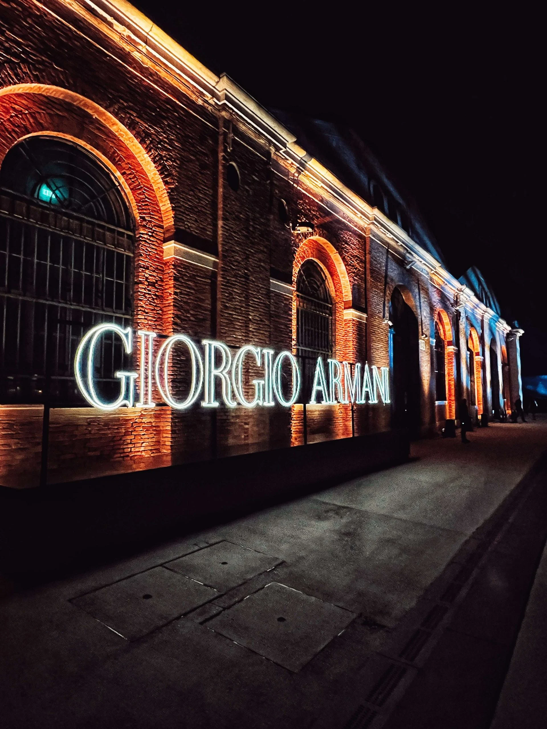 La scritta Giorgio Armani a lettere luminose davanti ai portici in mattoni dell'Arsenale di notte – Festa Armani/Archivio alla Mostra del Cinema di Venezia, Italia, 2025 – progettazione di eventi