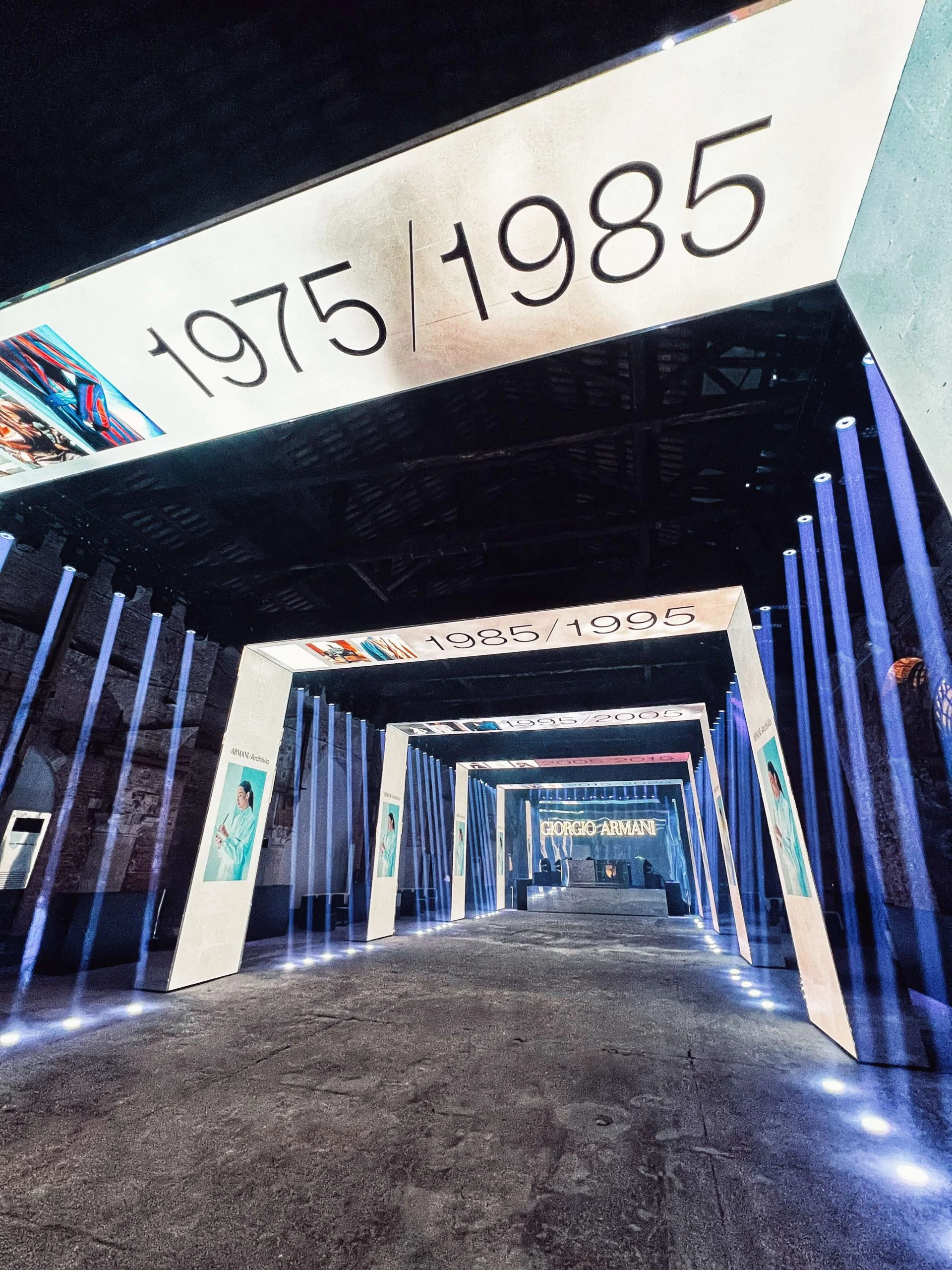 Vista dal basso attraverso il portale 1975/1985 lungo il corridoio fiancheggiato da tubi di luce blu verticali – Festa Armani/Archivio alla Mostra del Cinema di Venezia, Italia, 2025 – progettazione di eventi