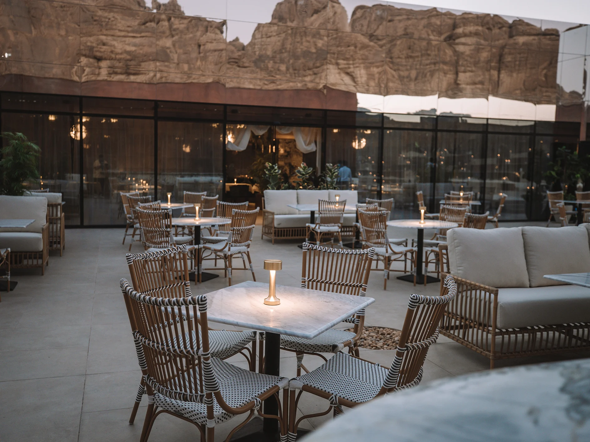 Terrazza del ristorante sul tetto al crepuscolo con tavoli illuminati, la parete a specchio che riflette rocce e una falesia – Maraya Concert Hall, AlUla, Arabia Saudita, 2019 – architettura