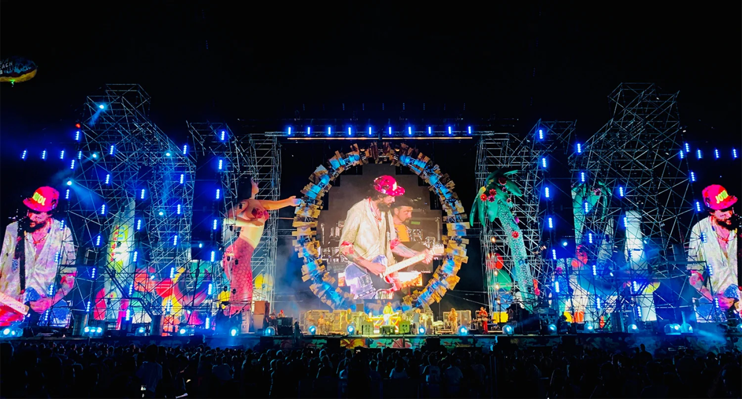 Vista notturna del palco del Jova Beach: torri di tubi illuminate di blu e schermi con il cantante dentro un anello colorato – Jova Beach Party 2022, Italia – scenografia per concerti