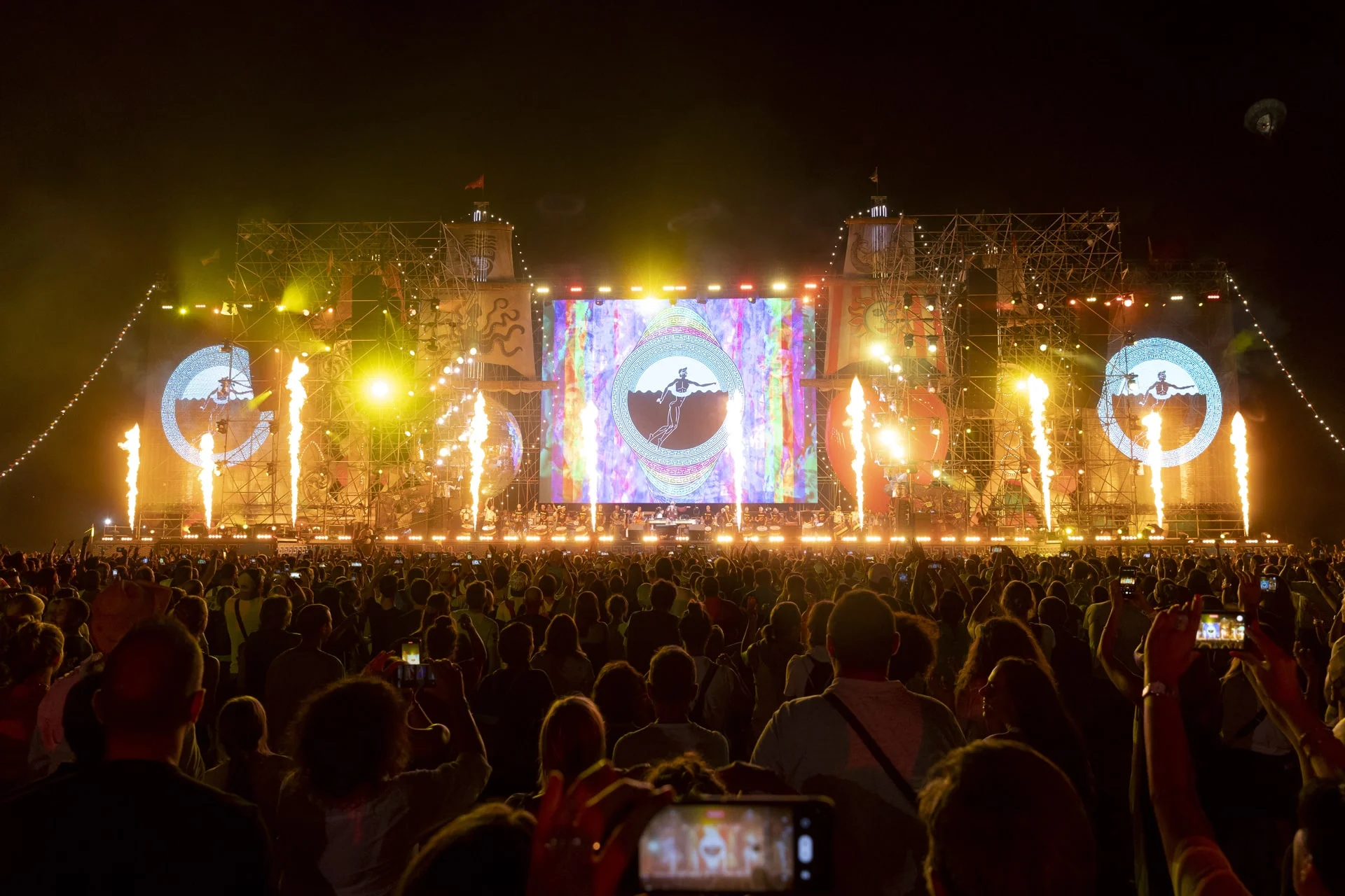 Getti di fiamme lungo il palco di notte, immagini psichedeliche sullo schermo centrale e sugli schermi laterali circolari – Jova Beach Party 2022, Italia – scenografia per concerti