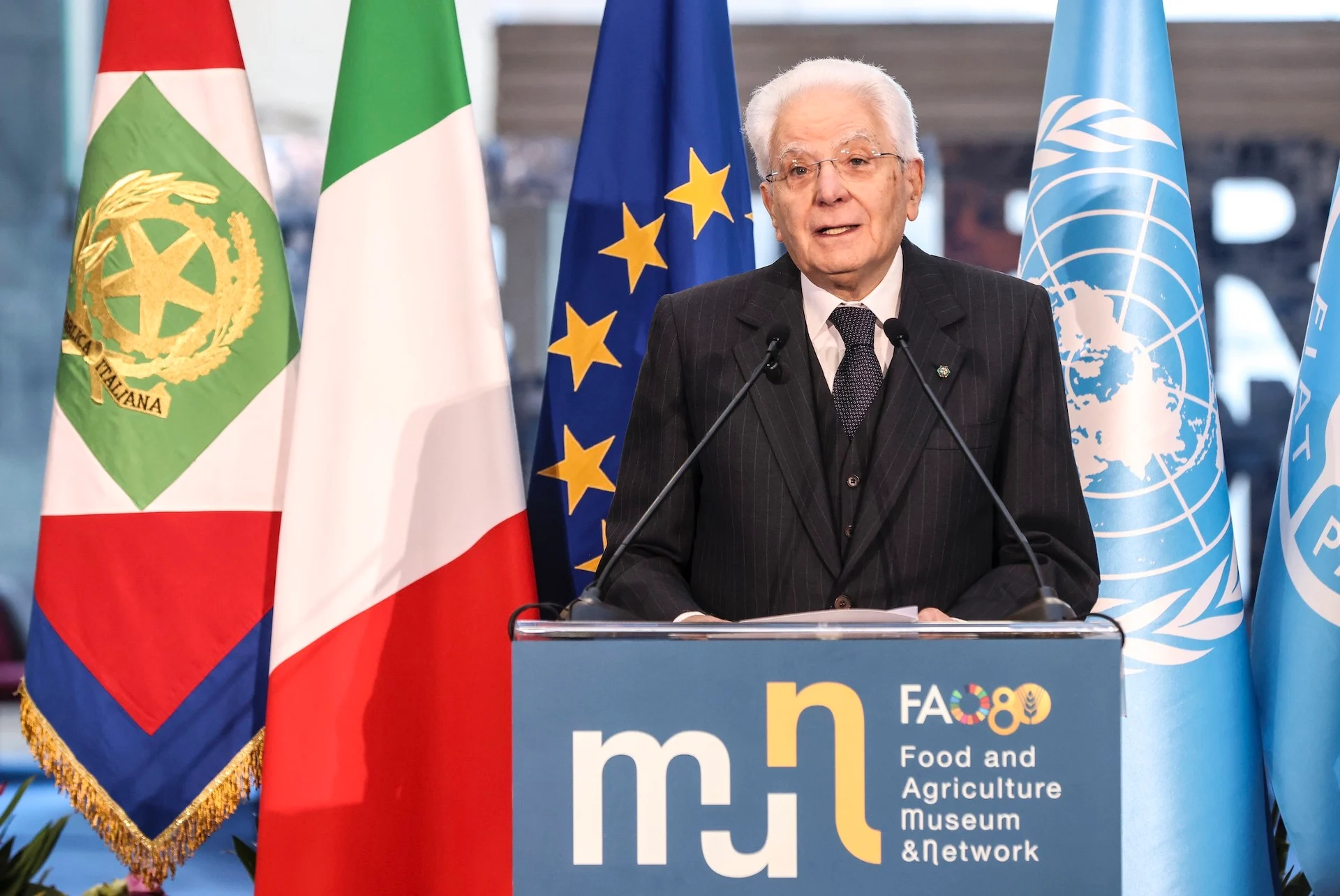 Oratore al podio del FAO MuNe davanti alle bandiere italiana, dell'UE e dell'ONU alla cerimonia di apertura – FAO MuNe Museo dell'alimentazione e dell'agricoltura, Roma, Italia, 2025 – allestimento espositivo
