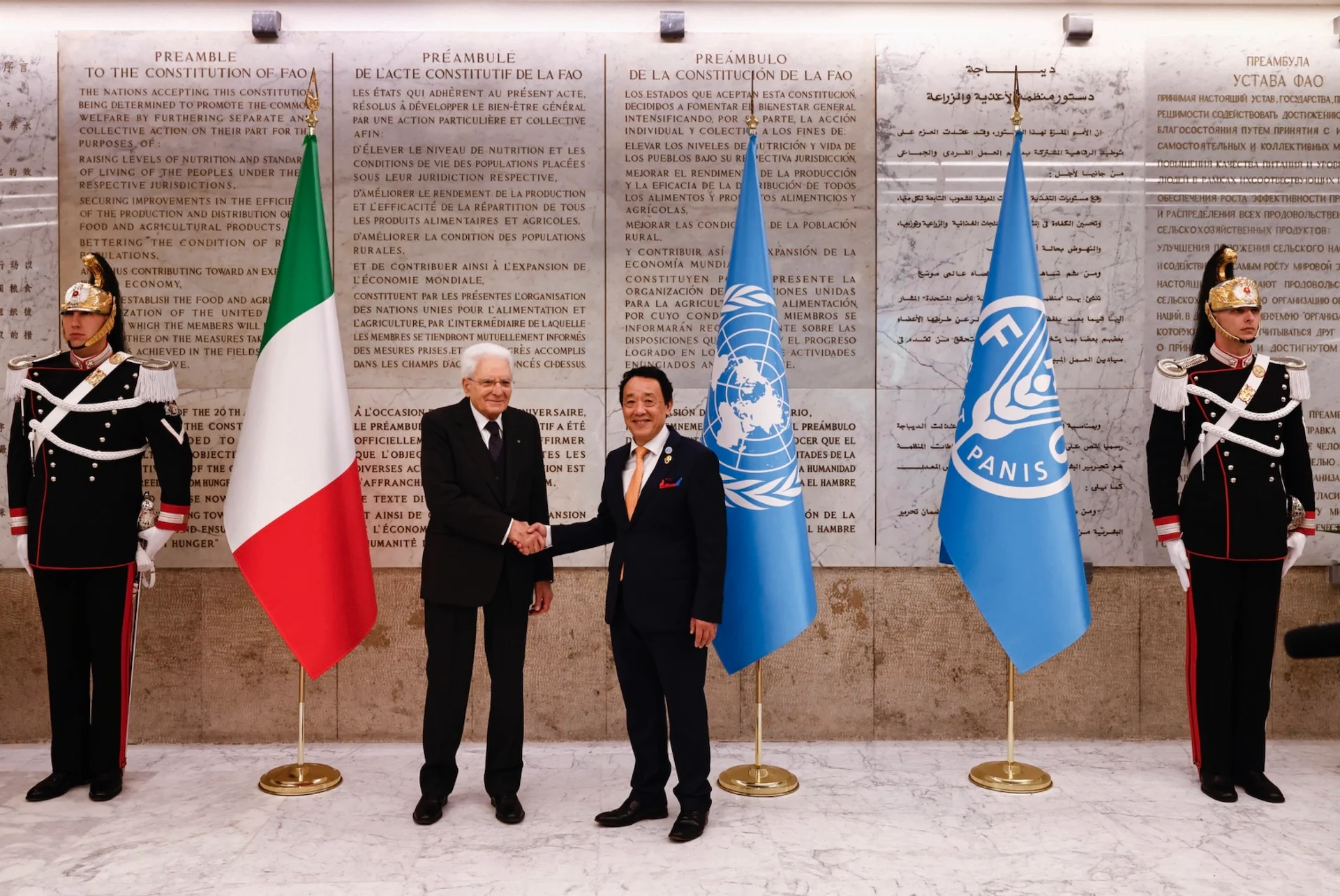 Due autorità si stringono la mano tra le bandiere italiana, dell'ONU e della FAO, guardie d'onore accanto alla parete del preambolo – FAO MuNe Museo dell'alimentazione e dell'agricoltura, Roma, Italia, 2025 – allestimento espositivo
