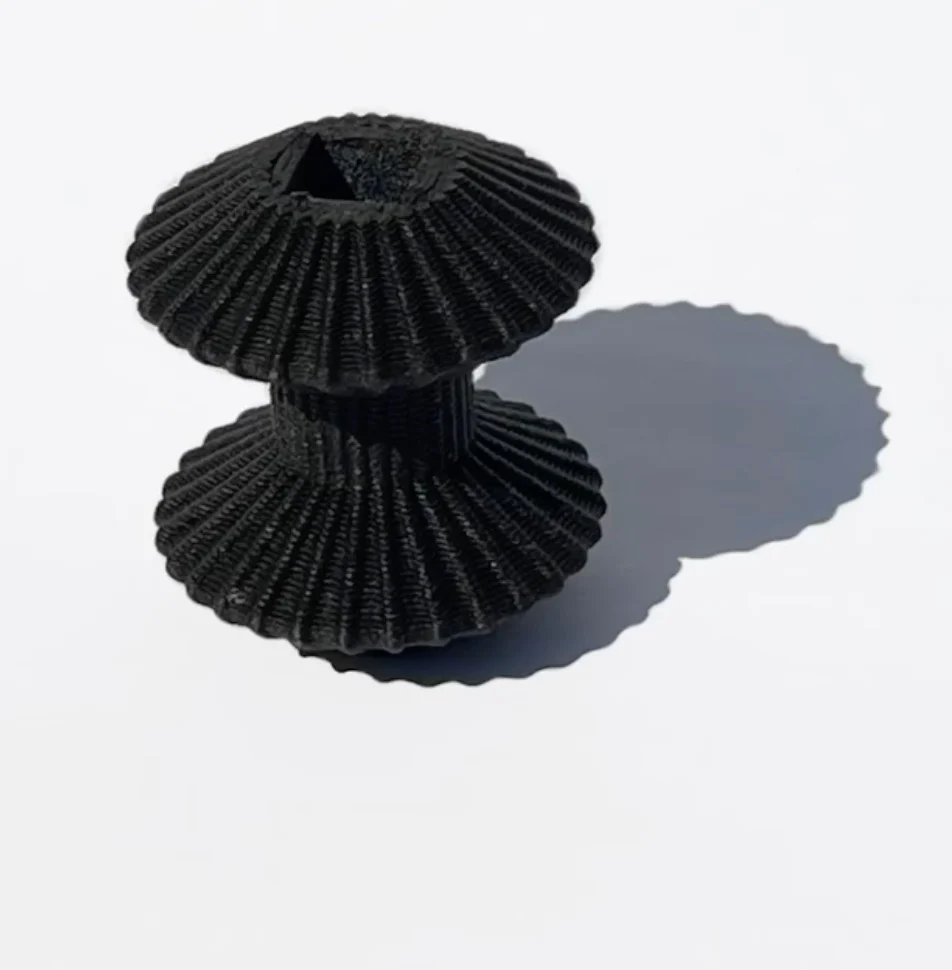 Pezzo nero stampato in 3D a forma di rocchetto con nervature su fondo bianco – Deep Surfaces a Palazzo Zorzi, Venezia, Italia, 2025 – allestimento espositivo