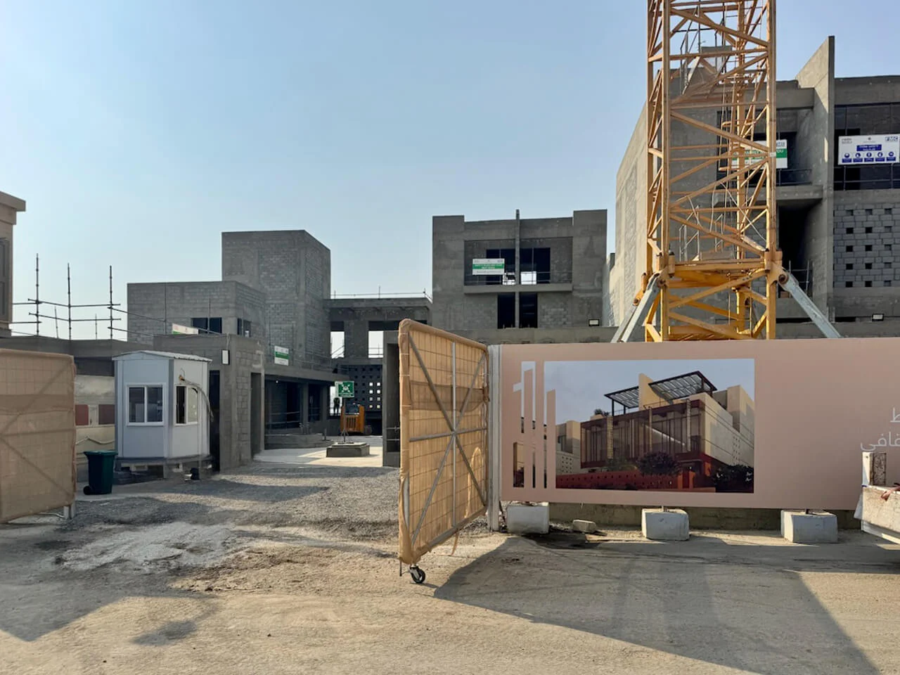 Ingresso del cantiere con le strutture in cemento delle ville, una gru a torre e una recinzione con il render del progetto – Radic Residences, Jeddah, Arabia Saudita, 2025 – architettura, in costruzione