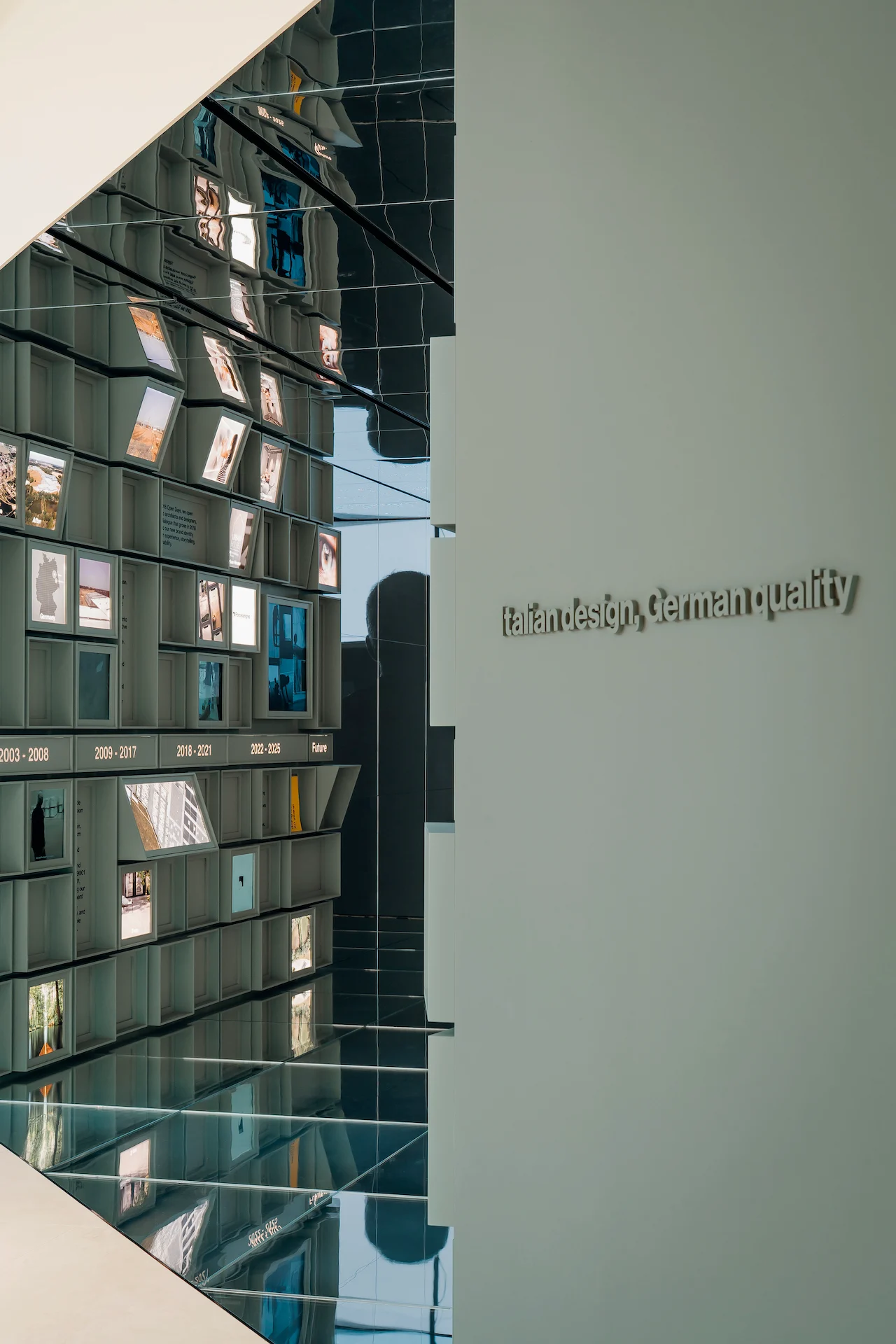 Ingresso a specchi con la parete modulare della linea del tempo e la scritta a parete Italian design, German quality – Porcelaingres Brand Narrative Space, Castellarano, Italia, 2025 – progettazione di showroom