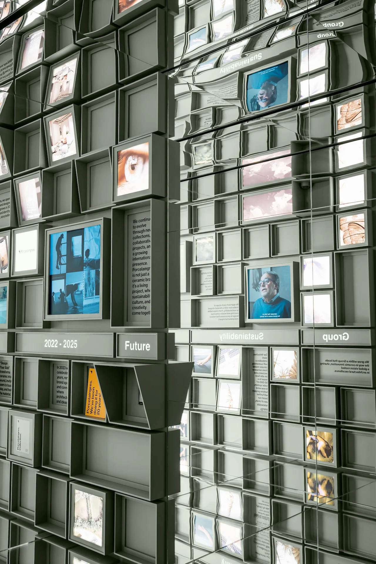 Parete di cubi con ritratti e schermi video riflessi nel soffitto e nelle pareti laterali a specchio – Porcelaingres Brand Narrative Space, Castellarano, Italia, 2025 – progettazione di showroom