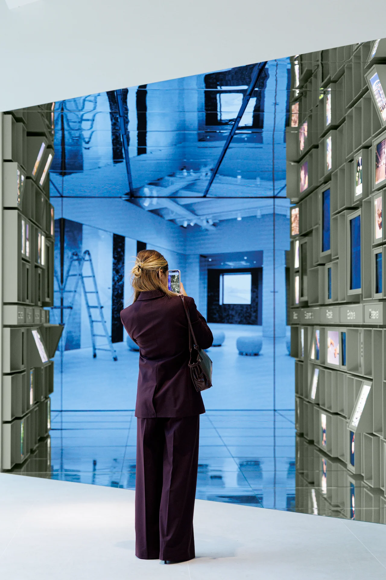 Visitatore che fotografa un grande videowall in fondo al passaggio a specchi – Porcelaingres Brand Narrative Space, Castellarano, Italia, 2025 – progettazione di showroom