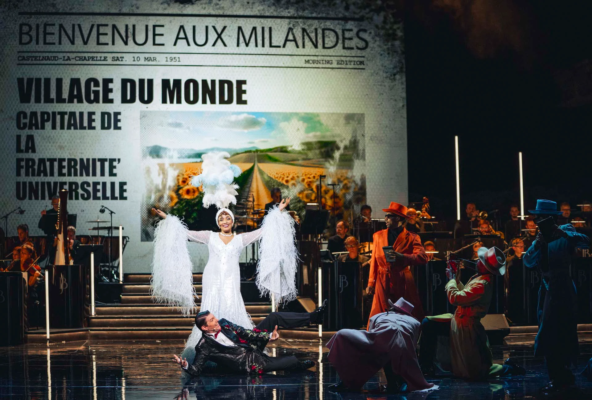 Cantante in costume bianco di piume davanti a una gigantesca pagina di giornale con la scritta Bienvenue aux Milandes – Bonsoir Monte-Carlo, Monte Carlo, Principato di Monaco, 2025 – scenografia
