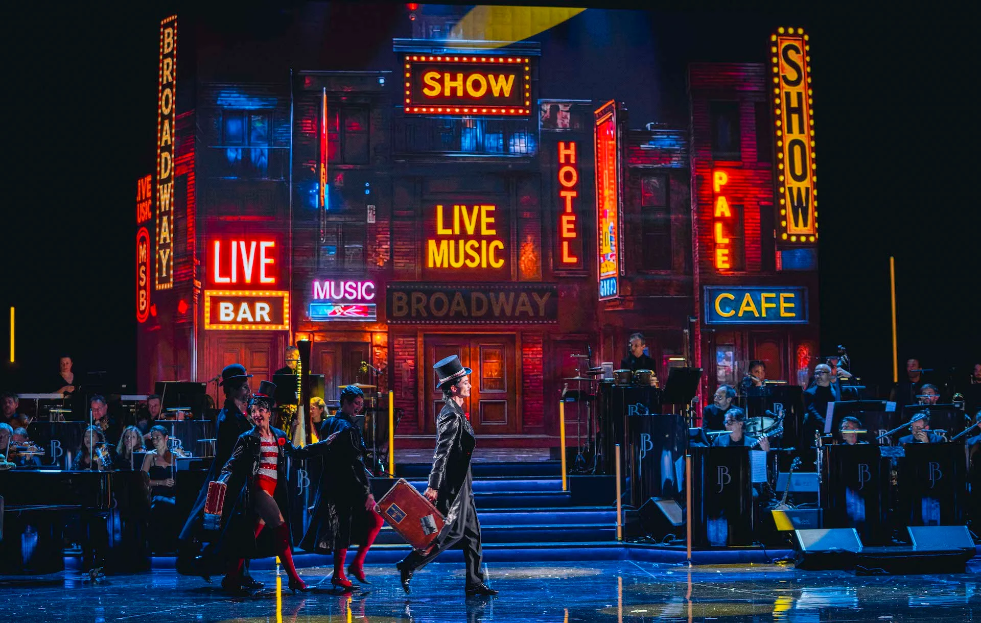 Artisti in cilindro che attraversano il palco davanti a un fondale di Broadway con insegne al neon, orchestra ai lati – Bonsoir Monte-Carlo, Monte Carlo, Principato di Monaco, 2025 – scenografia