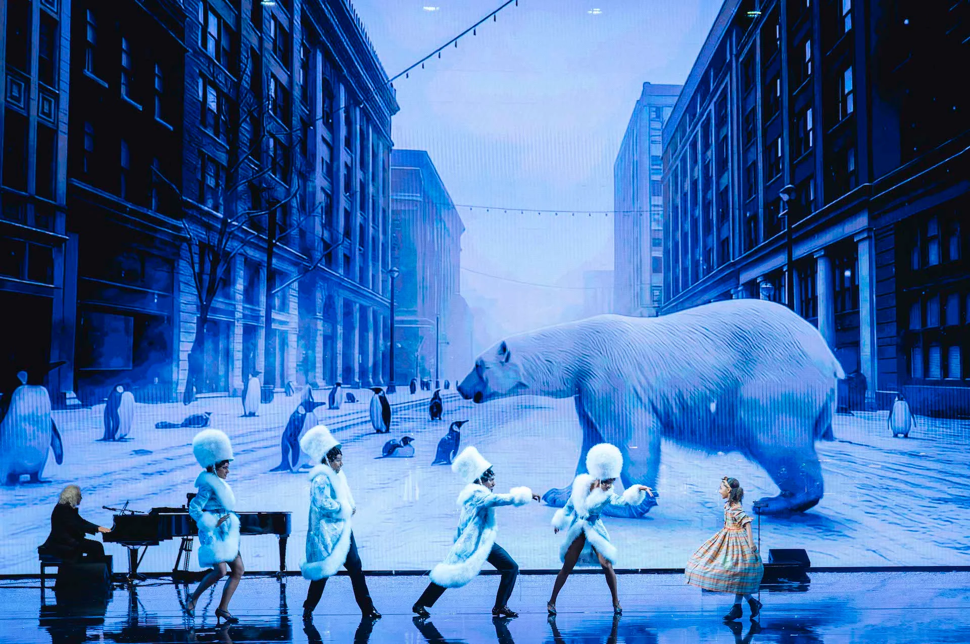 Ballerini in costumi di pelliccia bianca davanti alla proiezione di una strada innevata con un orso polare e pinguini – Bonsoir Monte-Carlo, Monte Carlo, Principato di Monaco, 2025 – scenografia
