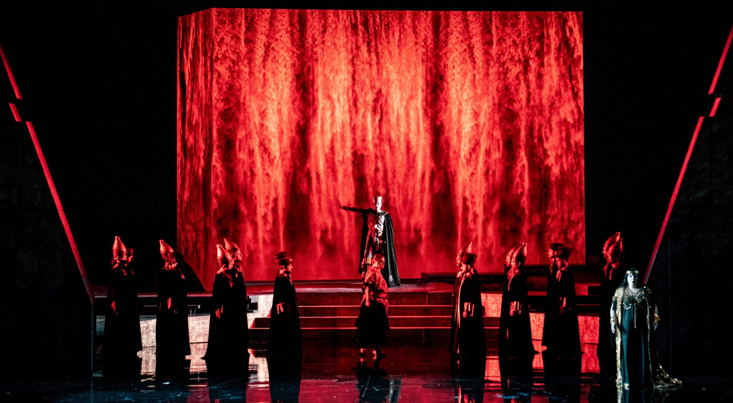 Blocco con proiezioni di texture rosso fuoco, sacerdoti con alti copricapi allineati davanti – Aida all'Opéra de Monte-Carlo, Principato di Monaco, 2025 – scenografia d'opera