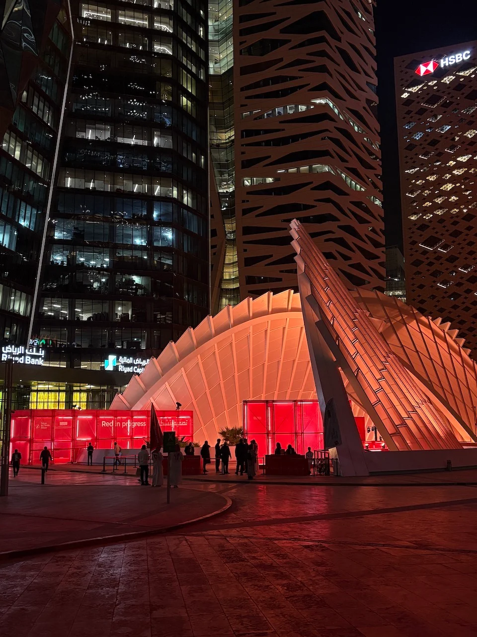 Vista notturna dell'installazione che brilla di rosso sotto una copertura illuminata tra le torri del KAFD a Riyadh – Red in Progress: Salone del Mobile Meets Riyadh, Arabia Saudita, 2025 – allestimento espositivo