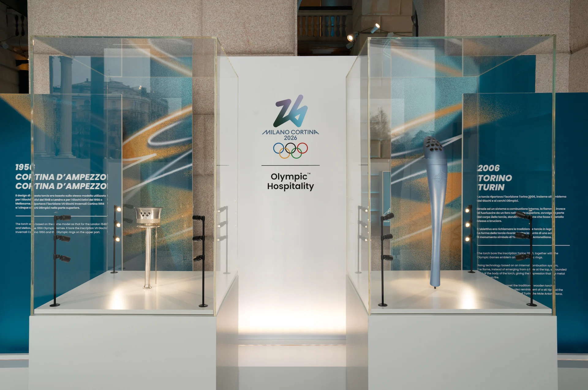 Teche con le torce olimpiche di Cortina 1956 e Torino 2006, ai lati di un pannello Milano Cortina 2026 – Clubhouse 26 Milano, Italia, 2026 – hospitality design