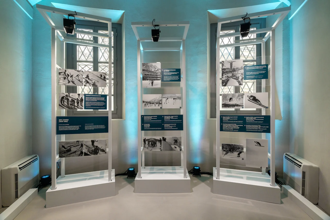 Tre telai bianchi con foto in bianco e nero di sport invernali storici, davanti ad alte finestre – Clubhouse 26 Milano, Italia, 2026 – hospitality design