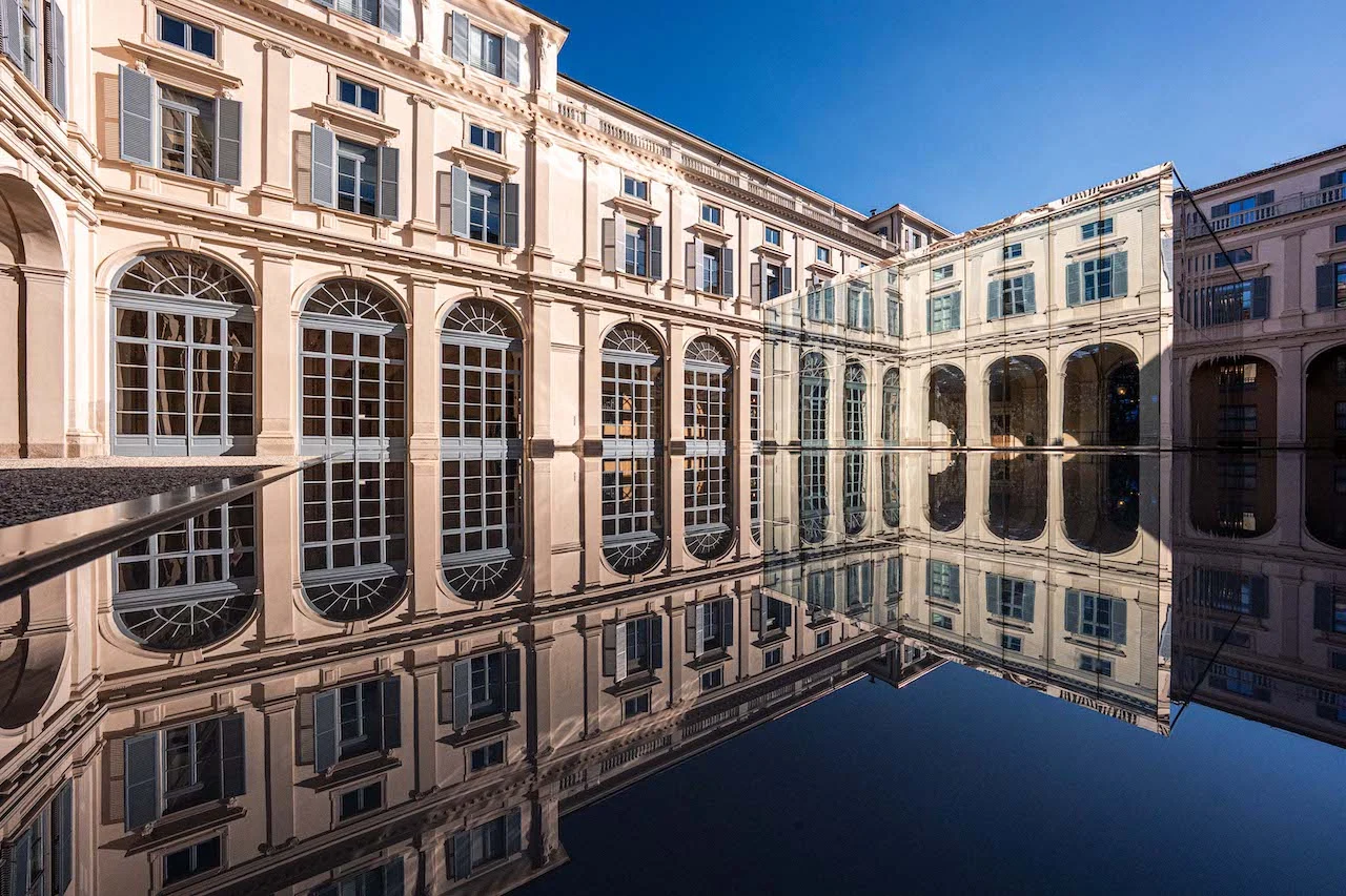 Facciate ad arcate del cortile di Palazzo Serbelloni riflesse nella vasca nera a specchio sotto un cielo blu – Samsung House a Palazzo Serbelloni, Milano, Italia, 2026 – interior design