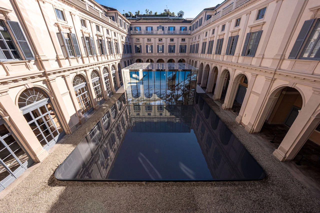 Vista aerea del cortile di Palazzo Serbelloni con un padiglione di vetro che emerge da una vasca nera a specchio – Samsung House a Palazzo Serbelloni, Milano, Italia, 2026 – interior design