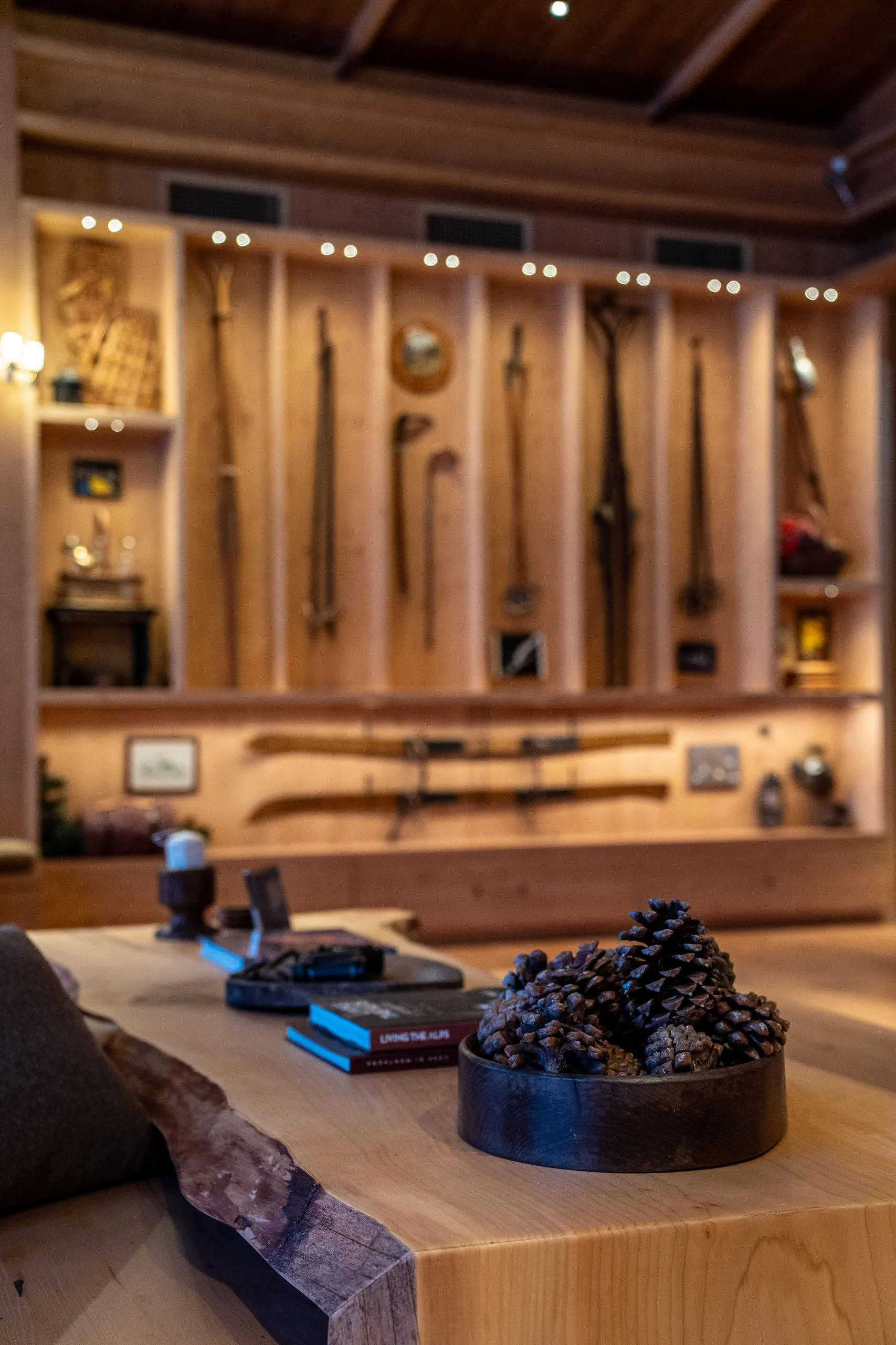 Tavolo in legno a bordo naturale con pigne davanti a un'esposizione illuminata di sci d'epoca e attrezzatura alpina – Samsung House a Palazzo Serbelloni, Milano, Italia, 2026 – interior design