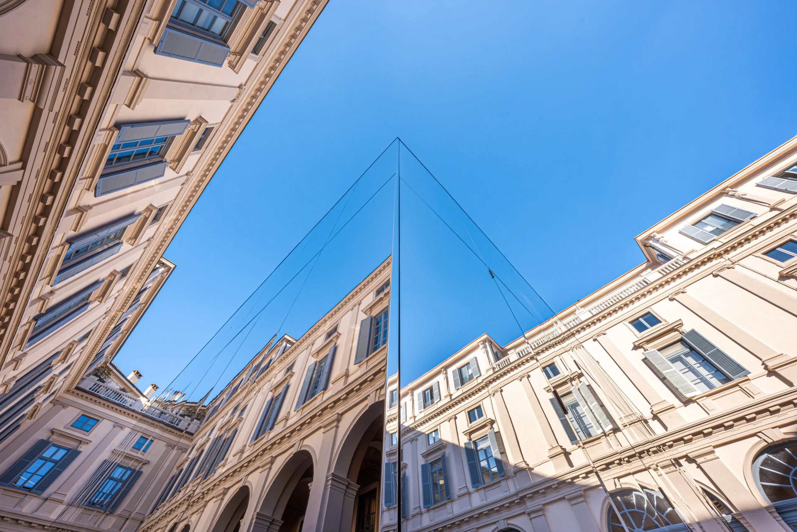 Vista dal basso dell'angolo del padiglione a specchio che riflette le facciate del palazzo contro un cielo azzurro limpido – Samsung House a Palazzo Serbelloni, Milano, Italia, 2026 – interior design