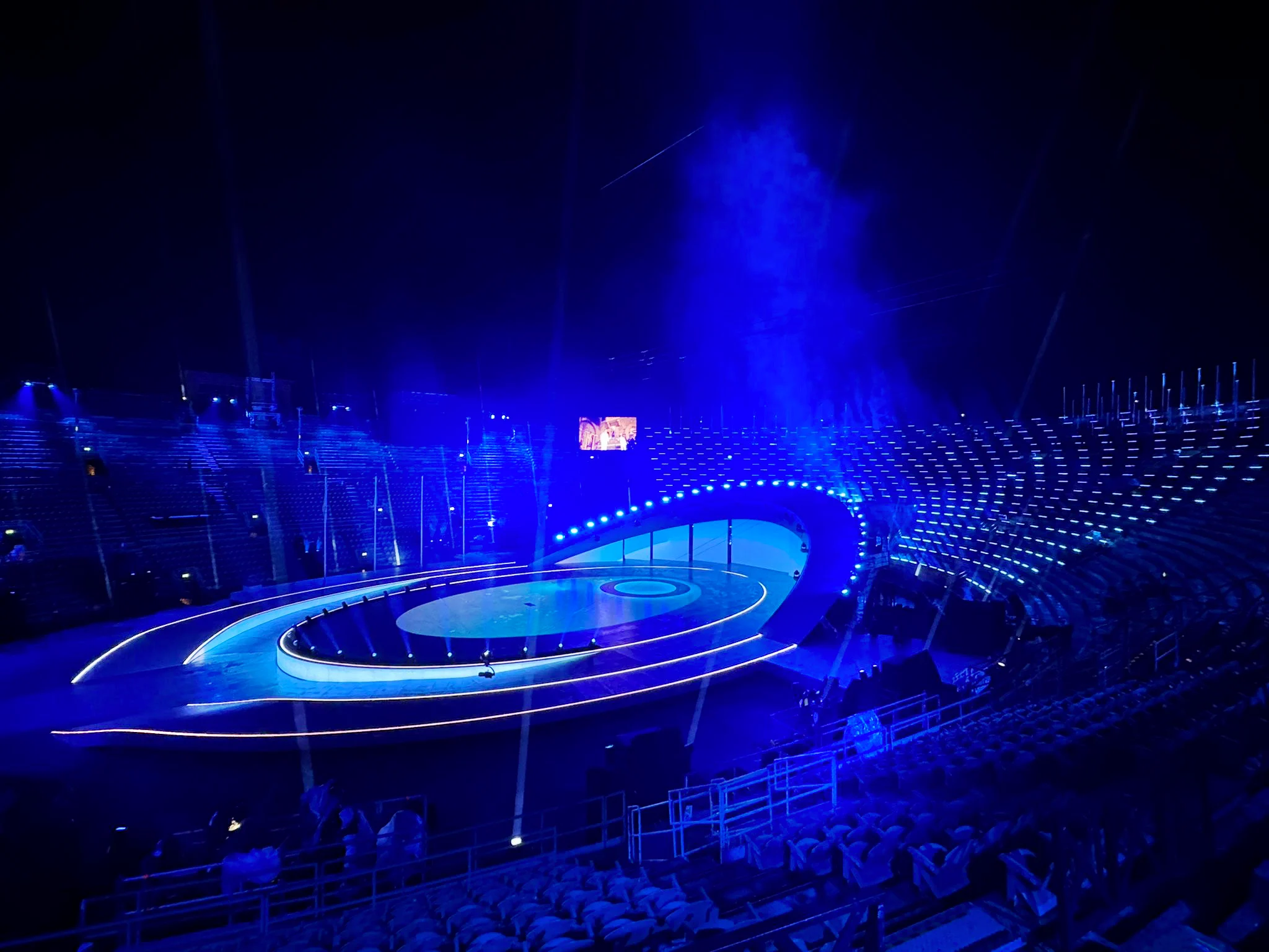 L'Arena di Verona vuota in luce blu, con il palco ovale e i suoi anelli profilati di LED – Cerimonia di chiusura dei Giochi Olimpici di Milano Cortina 2026, Verona, Italia – scenografia