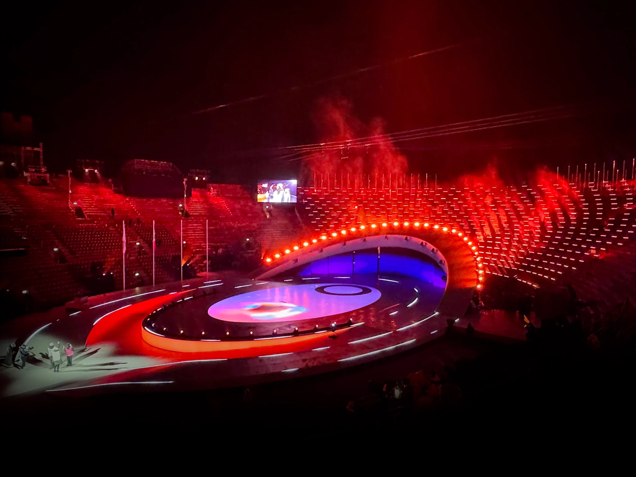 Palco e gradinate dell'arena immersi nella luce rossa, con una fila di luci lungo l'arco curvo – Cerimonia di chiusura dei Giochi Olimpici di Milano Cortina 2026, Verona, Italia – scenografia