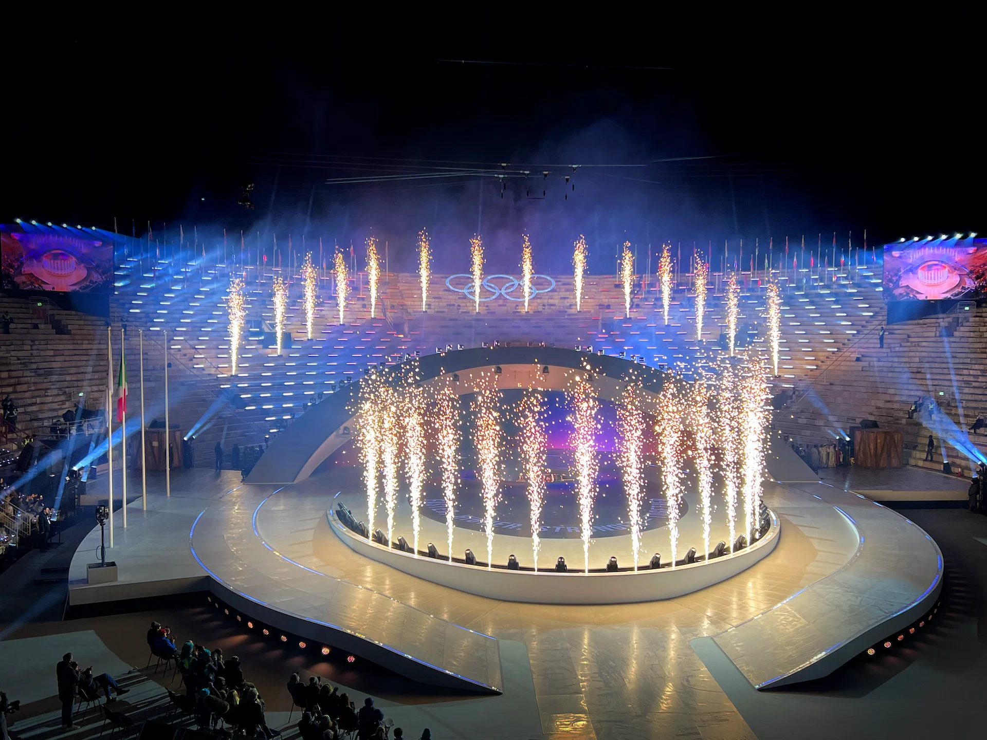 Fontane di scintille lungo il palco centrale e le gradinate dell'arena sotto gli anelli olimpici – Cerimonia di chiusura dei Giochi Olimpici di Milano Cortina 2026, Verona, Italia – scenografia