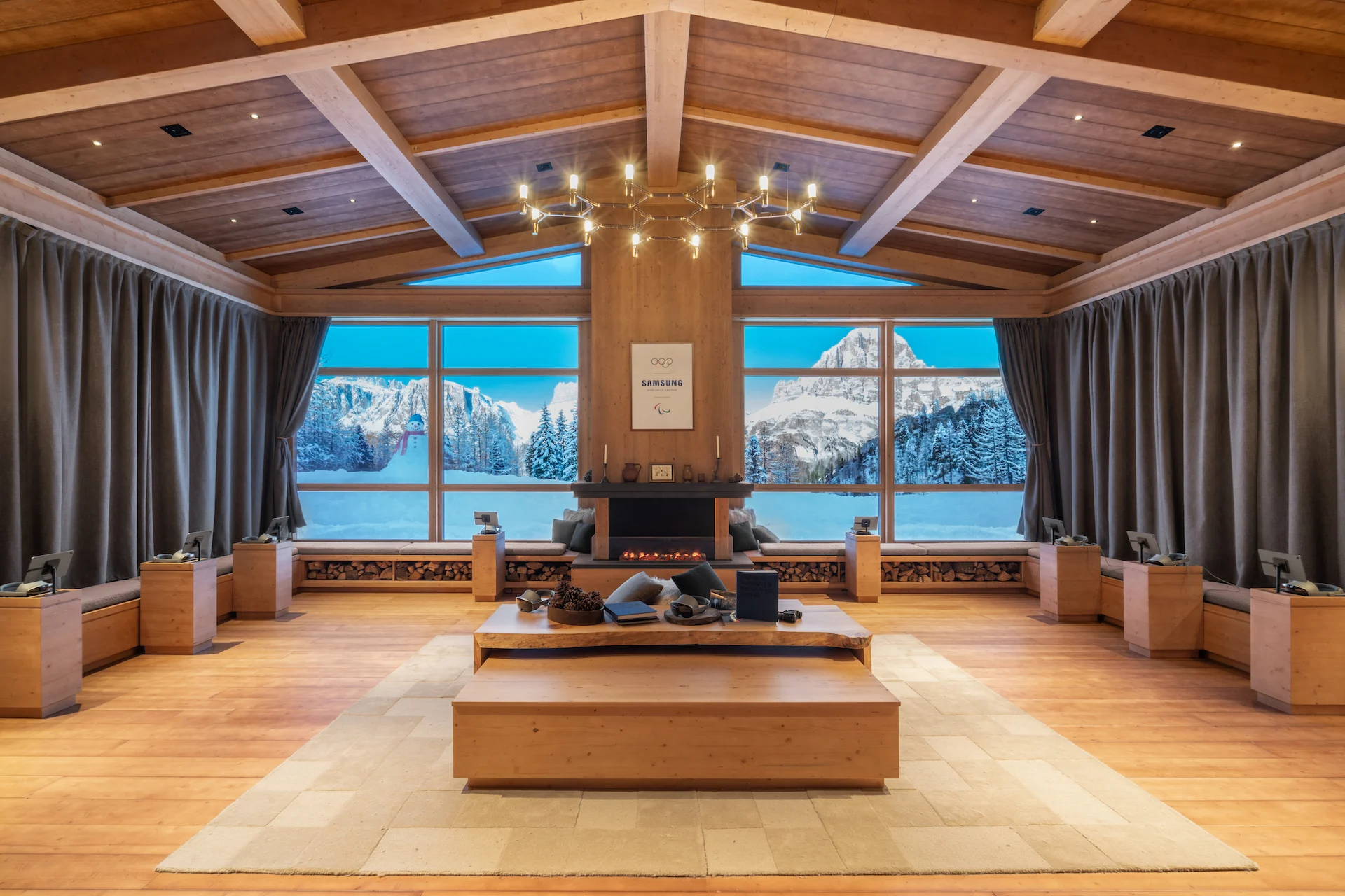 Lounge in stile alpino con soffitto in legno, camino e grandi finestre che inquadrano le montagne innevate – Samsung House a Palazzo Serbelloni, Milano, Italia, 2026 – interior design