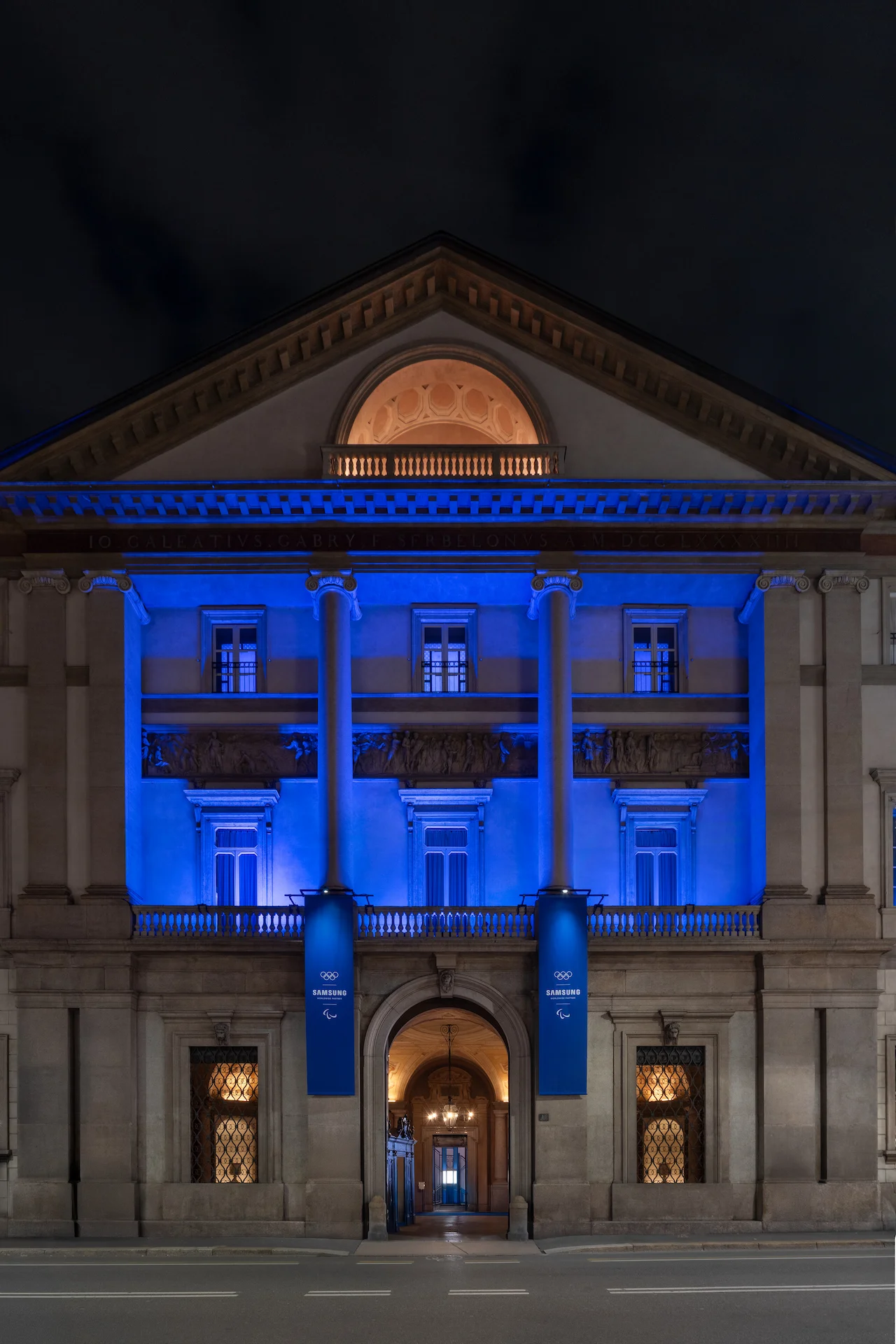 Facciata di Palazzo Serbelloni di notte immersa nella luce blu, stendardi Samsung all'ingresso – Samsung House a Palazzo Serbelloni, Milano, Italia, 2026 – interior design