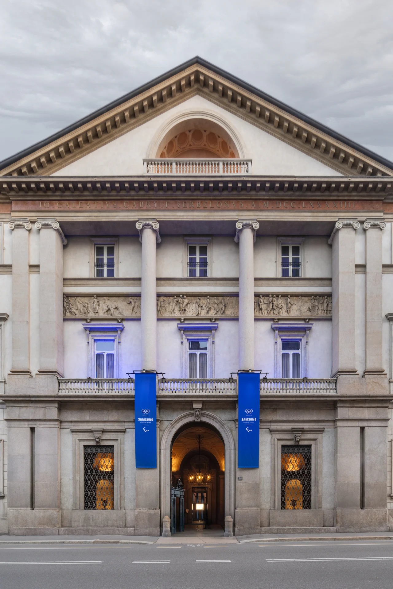 Facciata neoclassica di Palazzo Serbelloni di giorno, due stendardi blu Samsung accanto all'ingresso – Samsung House a Palazzo Serbelloni, Milano, Italia, 2026 – interior design