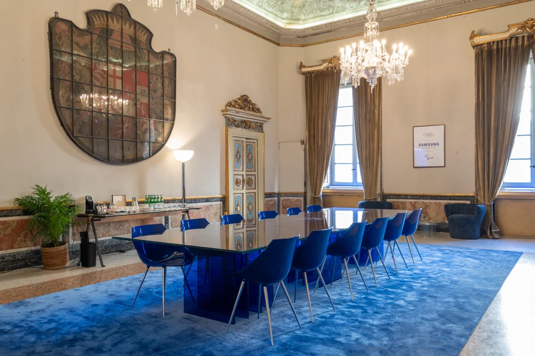 Tavolo in vetro STRACTA con sedie blu come tavolo riunioni in un salone affrescato con lampadari – Tavolo STRACTA per Driade, Milano, Italia, 2026 – design di prodotto