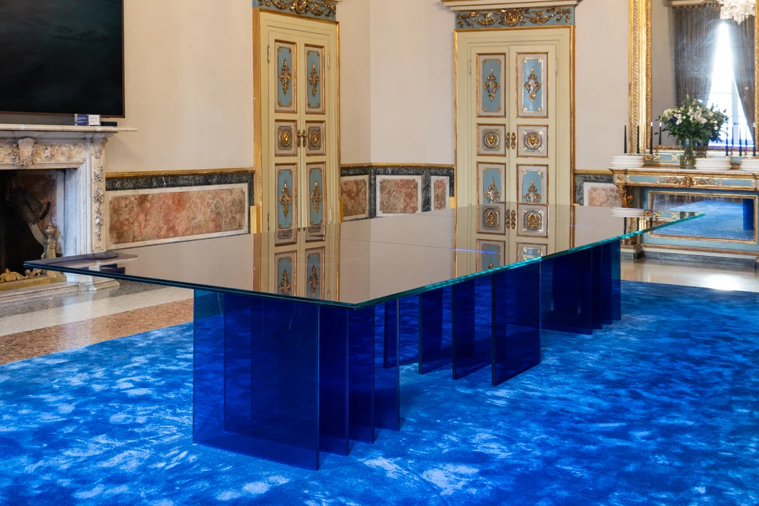 Tavolo STRACTA ad altezza d'occhio, con il piano in vetro che riflette porte dipinte e un camino in marmo accanto – Tavolo STRACTA per Driade, Milano, Italia, 2026 – design di prodotto