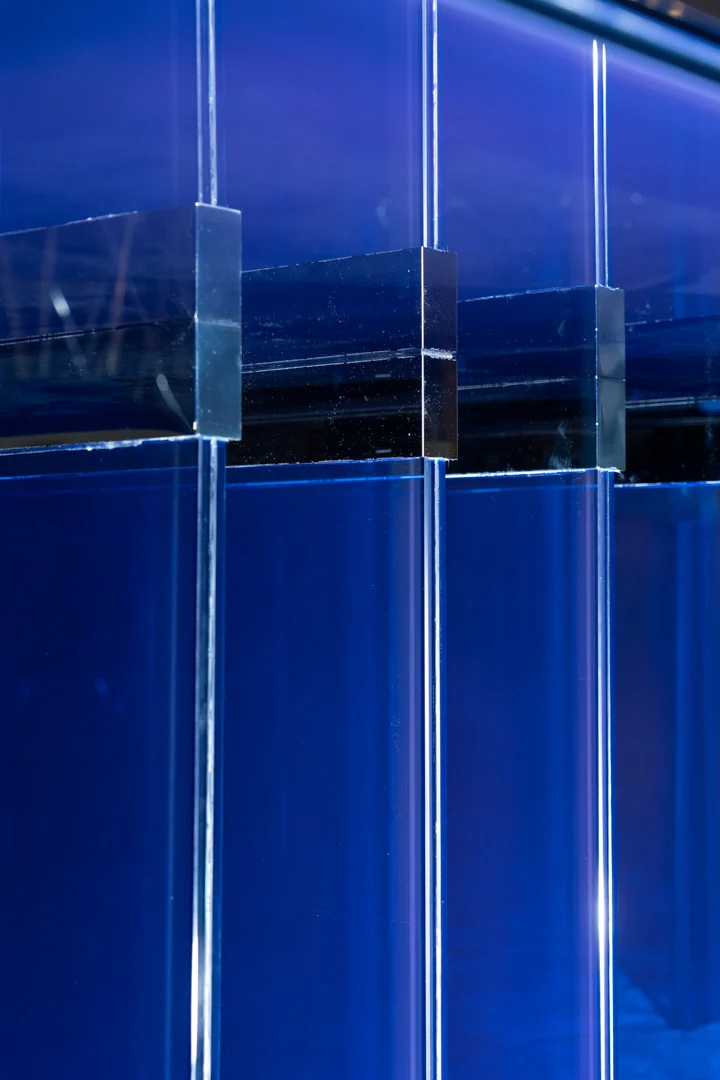 Dettaglio dei blocchetti di giunzione in vetro tra i pannelli stratificati in vetro blu della base del tavolo – Tavolo STRACTA per Driade, Milano, Italia, 2026 – design di prodotto
