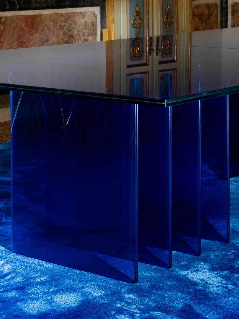 Angolo del tavolo STRACTA: piano in vetro trasparente appoggiato su pannelli sfalsati in vetro blu – Tavolo STRACTA per Driade, Milano, Italia, 2026 – design di prodotto