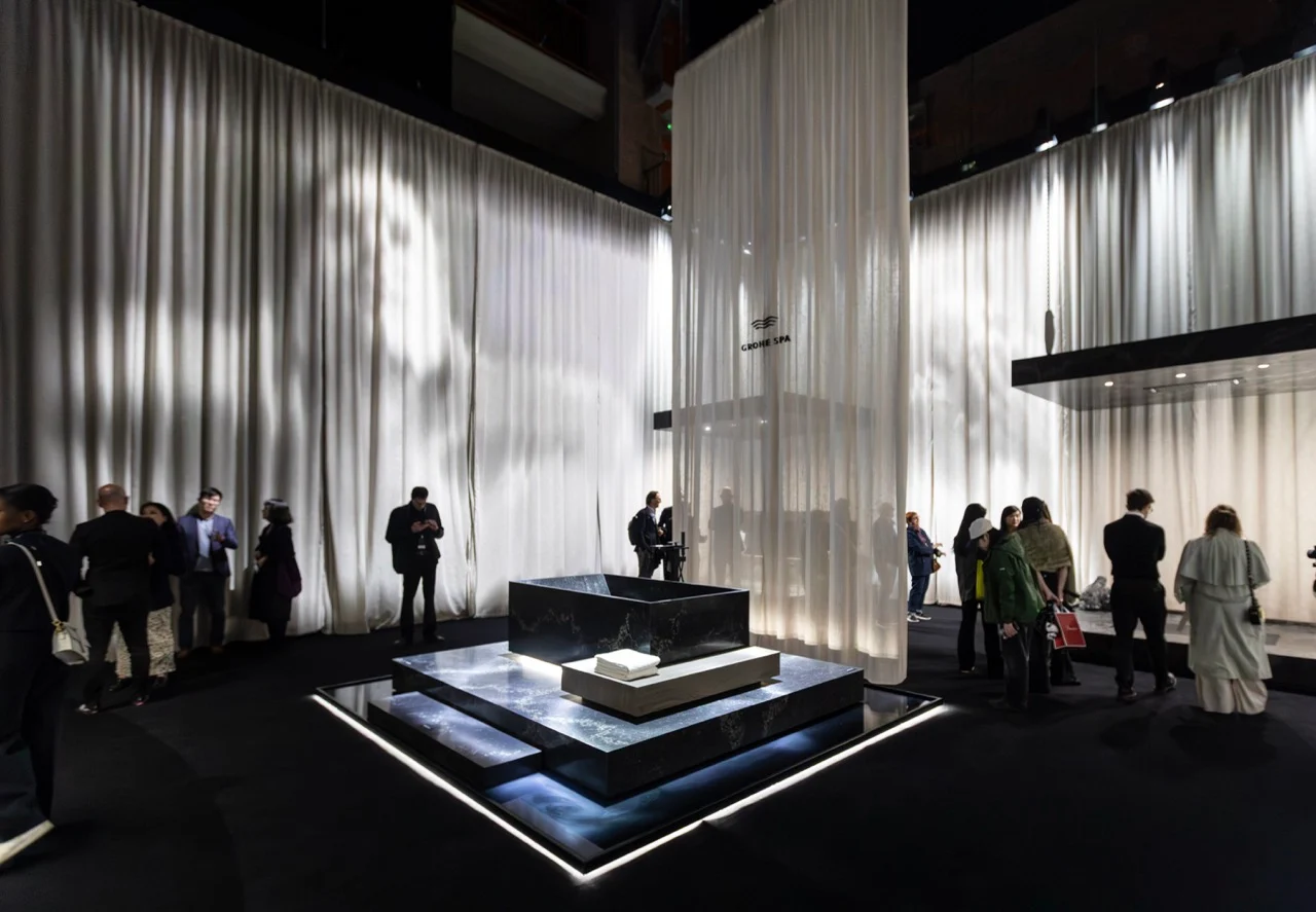 GROHE SPA Aqua Sanctuary: vasca in pietra scura su una pedana illuminata, circondata da alte tende bianche e visitatori – GROHE SPA Aqua Sanctuary al Fuorisalone, Milano, Italia, 2026 – progettazione di installazioni