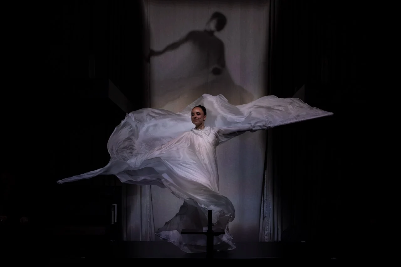 Ballerina che fa vorticare un tessuto bianco fluttuante su un palco buio, la sua ombra proiettata sulla tenda dietro – GROHE SPA Aqua Sanctuary al Fuorisalone, Milano, Italia, 2026 – progettazione di installazioni