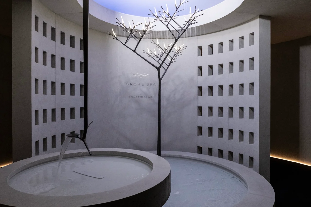Sala spa circolare con pareti traforate, vasche d'acqua rotonde e una doccia a forma di albero sotto un lucernario – GROHE SPA Aqua Sanctuary al Fuorisalone, Milano, Italia, 2026 – progettazione di installazioni