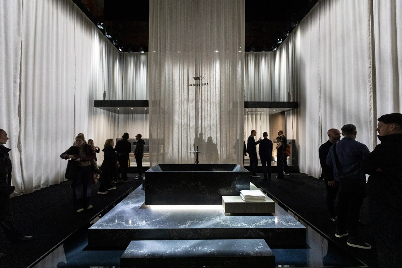 Vista in profondità della sala con tende e una vasca in pietra nera su un basamento illuminato, visitatori ai lati – GROHE SPA Aqua Sanctuary al Fuorisalone, Milano, Italia, 2026 – progettazione di installazioni
