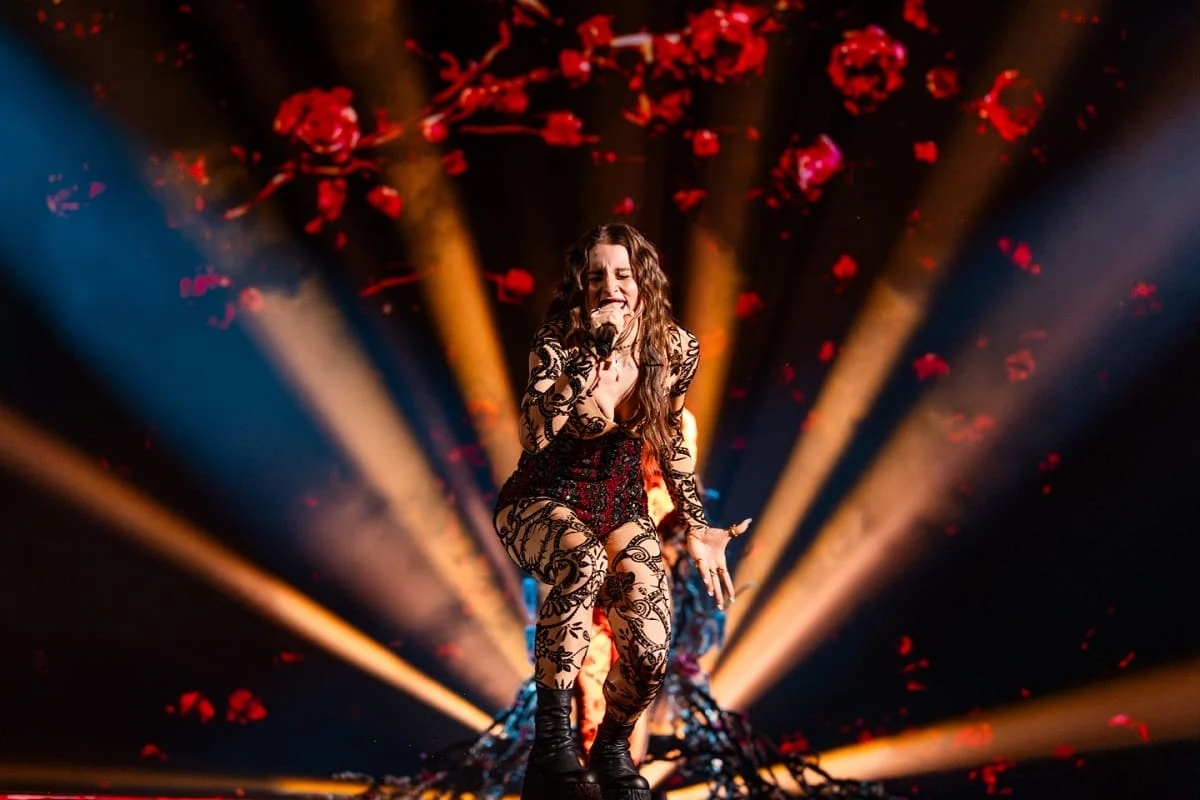 Cantante accovacciata durante l'esibizione sotto proiezioni di rose rosse e fasci di luce arancioni a ventaglio – Angelina Mango all'Eurovision 2024, Malmö, Svezia – scenografia per concerti