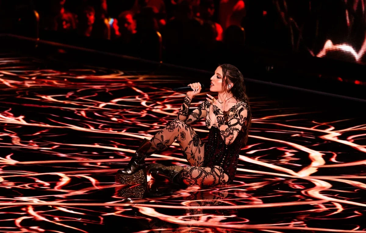 Angelina Mango seduta su un pavimento lucido attraversato da vortici di luce rossa e bianca, mentre canta al microfono – Angelina Mango all'Eurovision 2024, Malmö, Svezia – scenografia per concerti