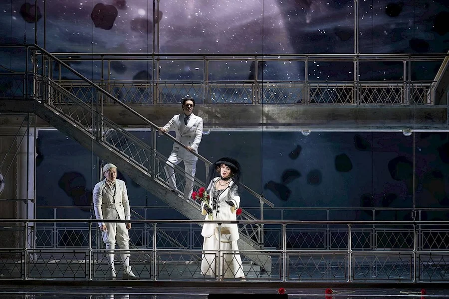 Tre cantanti in bianco sulle scale e sul ponte della scenografia contro un cielo stellato proiettato – Giulio Cesare in Egitto all'Opéra de Monte-Carlo, Principato di Monaco, 2025 – scenografia d'opera