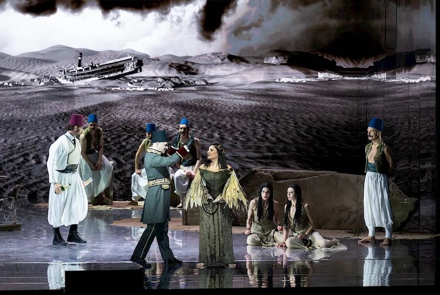 Cantanti in costume e fez davanti alla proiezione di un deserto con un battello a vapore arenato – Giulio Cesare in Egitto all'Opéra de Monte-Carlo, Principato di Monaco, 2025 – scenografia d'opera