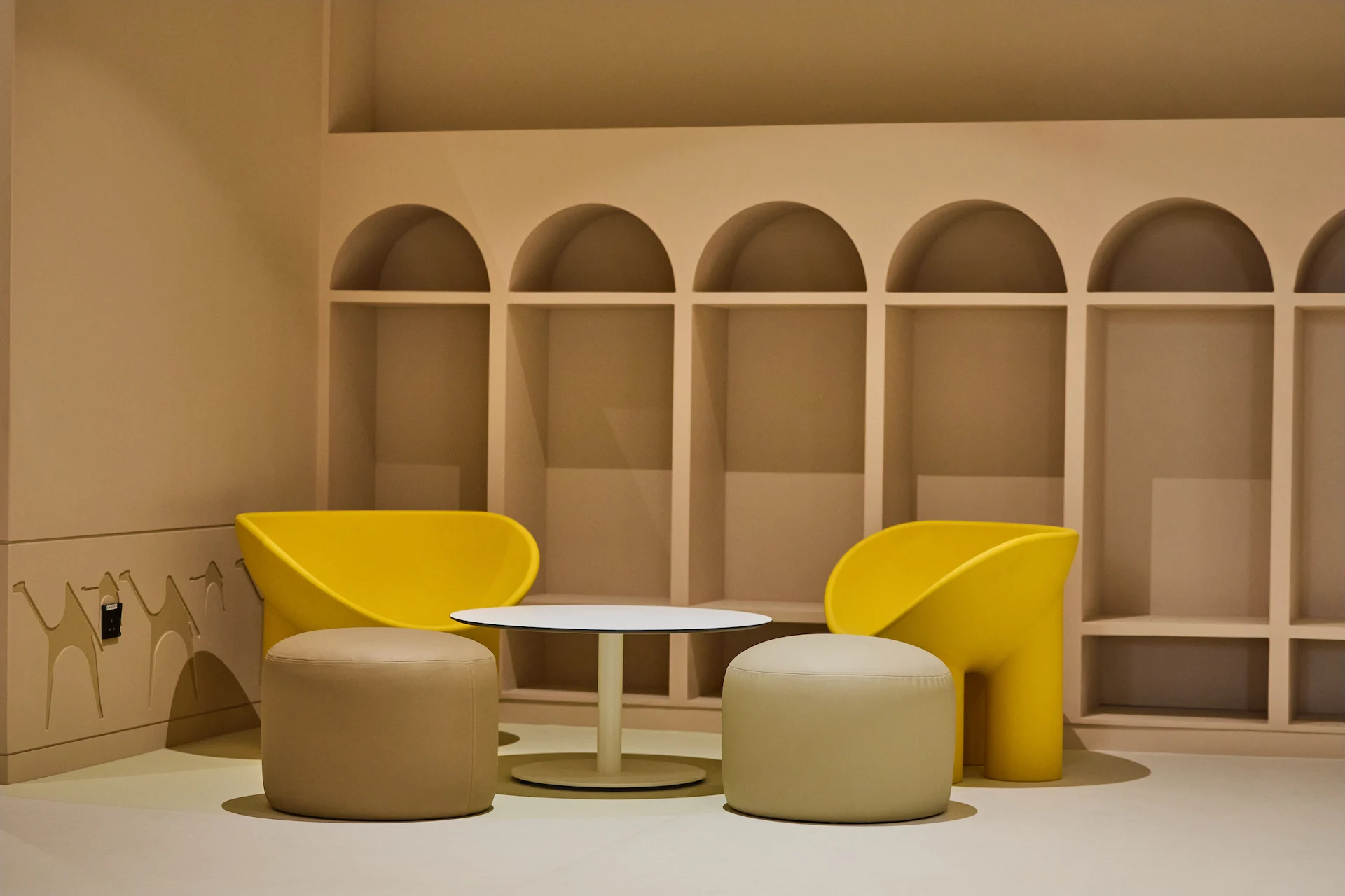 Angolo lounge con poltrone gialle e pouf rotondi davanti a nicchie ad arco in una parete color sabbia – Sede del MOC, Diriyah, Arabia Saudita, 2026 – interior design
