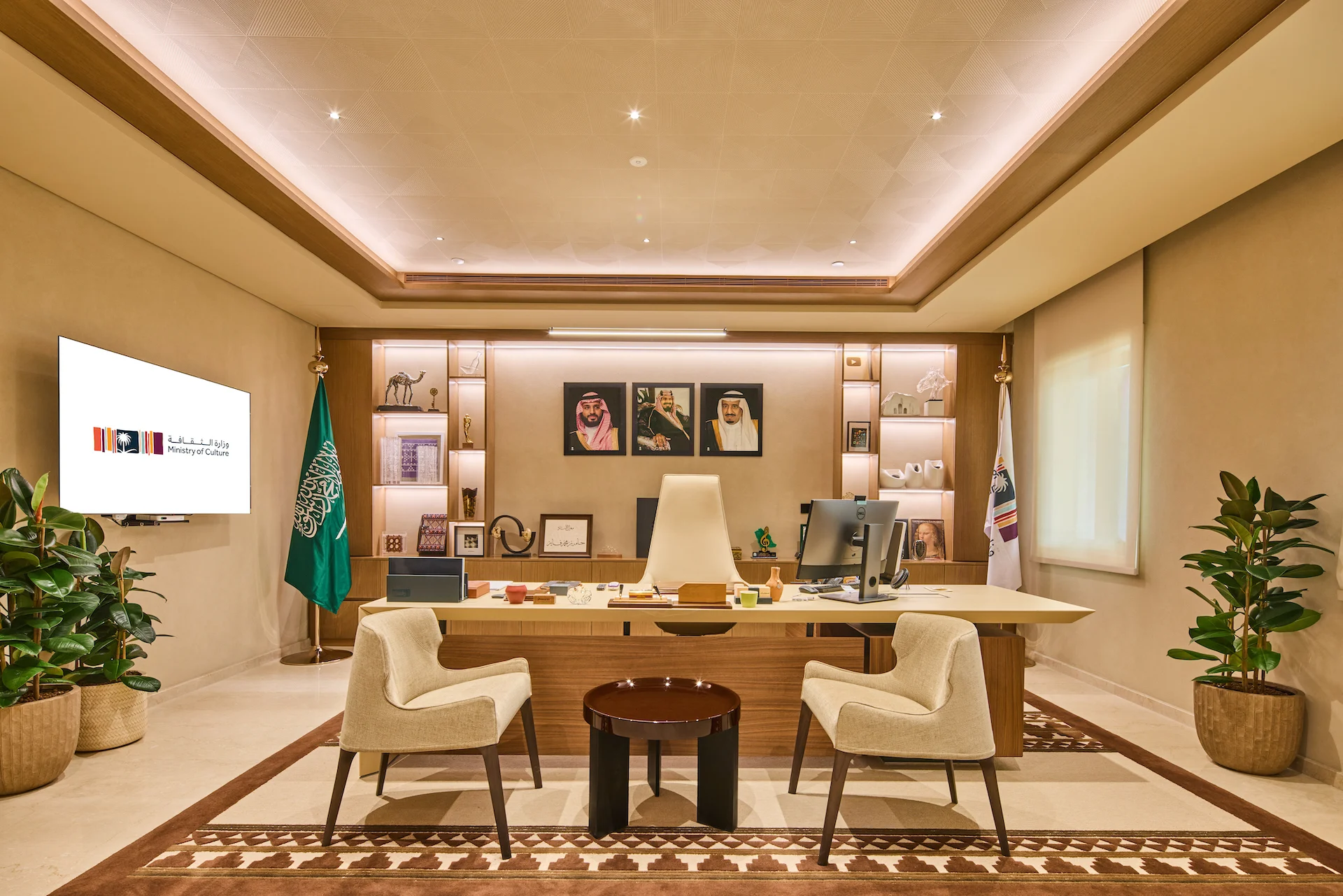 Ufficio direzionale con scrivania in legno, scaffali retroilluminati, ritratti incorniciati, bandiere e un tappeto decorato – Sede del MOC, Diriyah, Arabia Saudita, 2026 – interior design