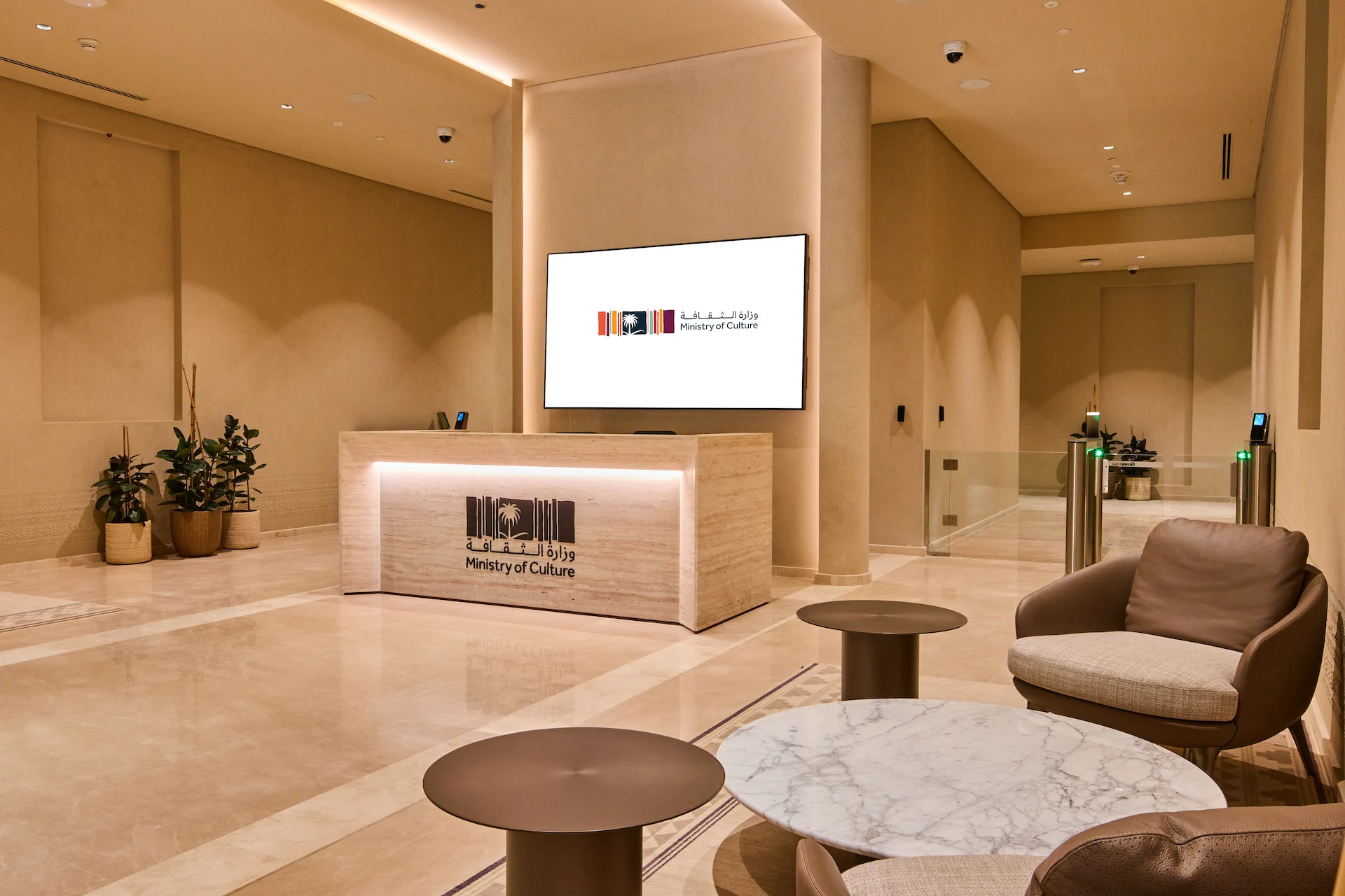 Reception del Ministero della Cultura: bancone in travertino con logo, schermo a parete e poltrone attorno a tavolini in marmo – Sede del MOC, Diriyah, Arabia Saudita, 2026 – interior design