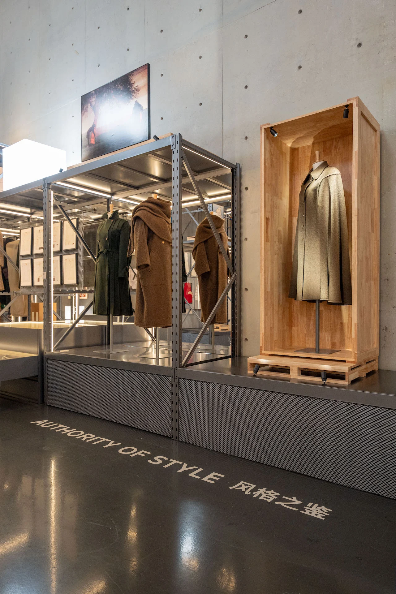 Sezione Authority of Style: cappotti su scaffalature metalliche e un unico cappotto in un'alta vetrina di legno – Max Mara The Max! al Long Museum, Shanghai, Cina, 2026 – allestimento espositivo